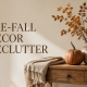 a minimally decorated table for the fall season with a pumpkin, candle and fall stems in a vase